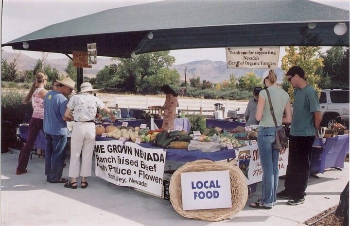 A Nevada farmers' market stall under an awning, with a Local Food sign and shoppers